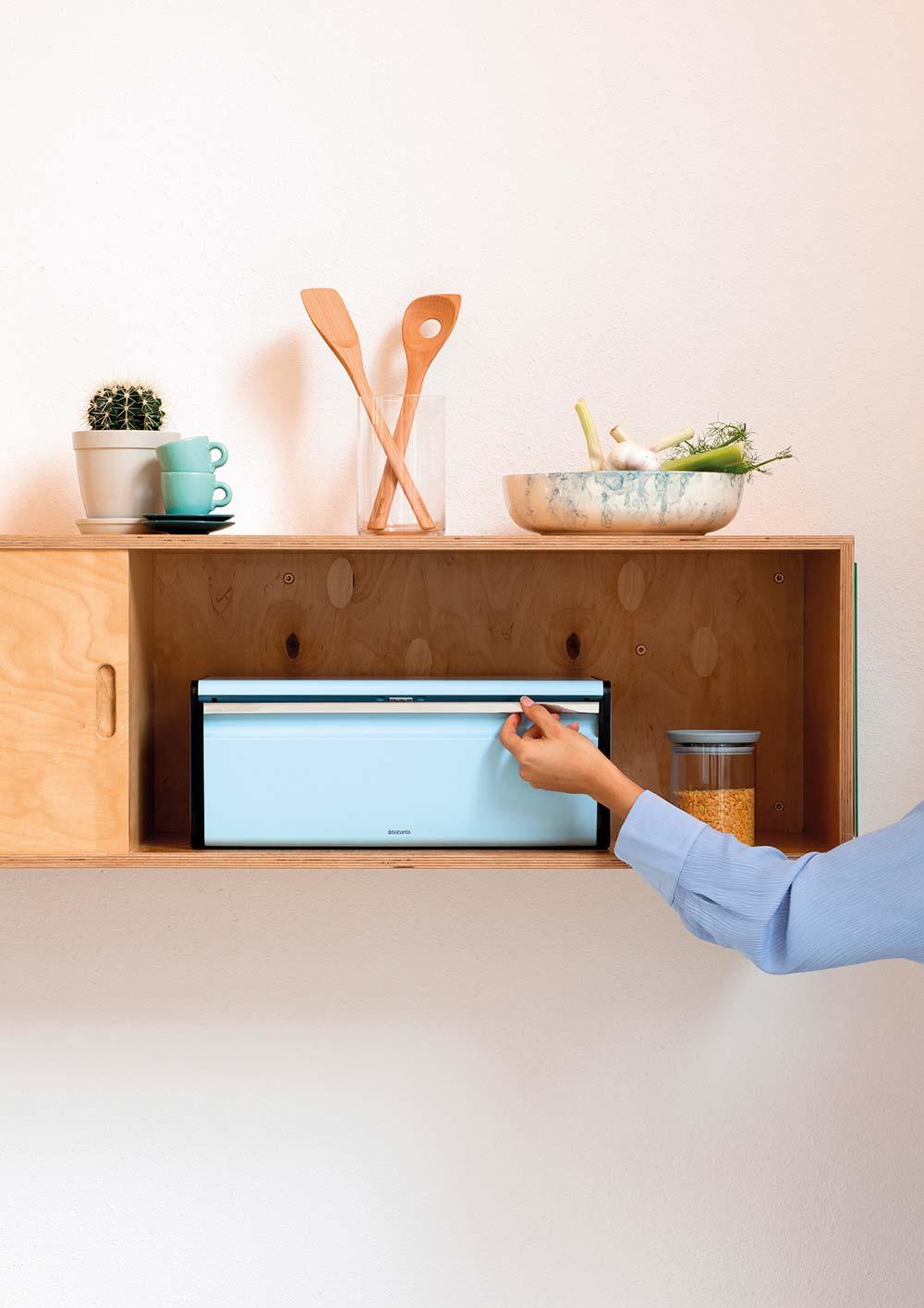 Minimalistische houten wandkast in een keuken met een geïntegreerde Brabantia broodtrommel en decoratieve accessoires.