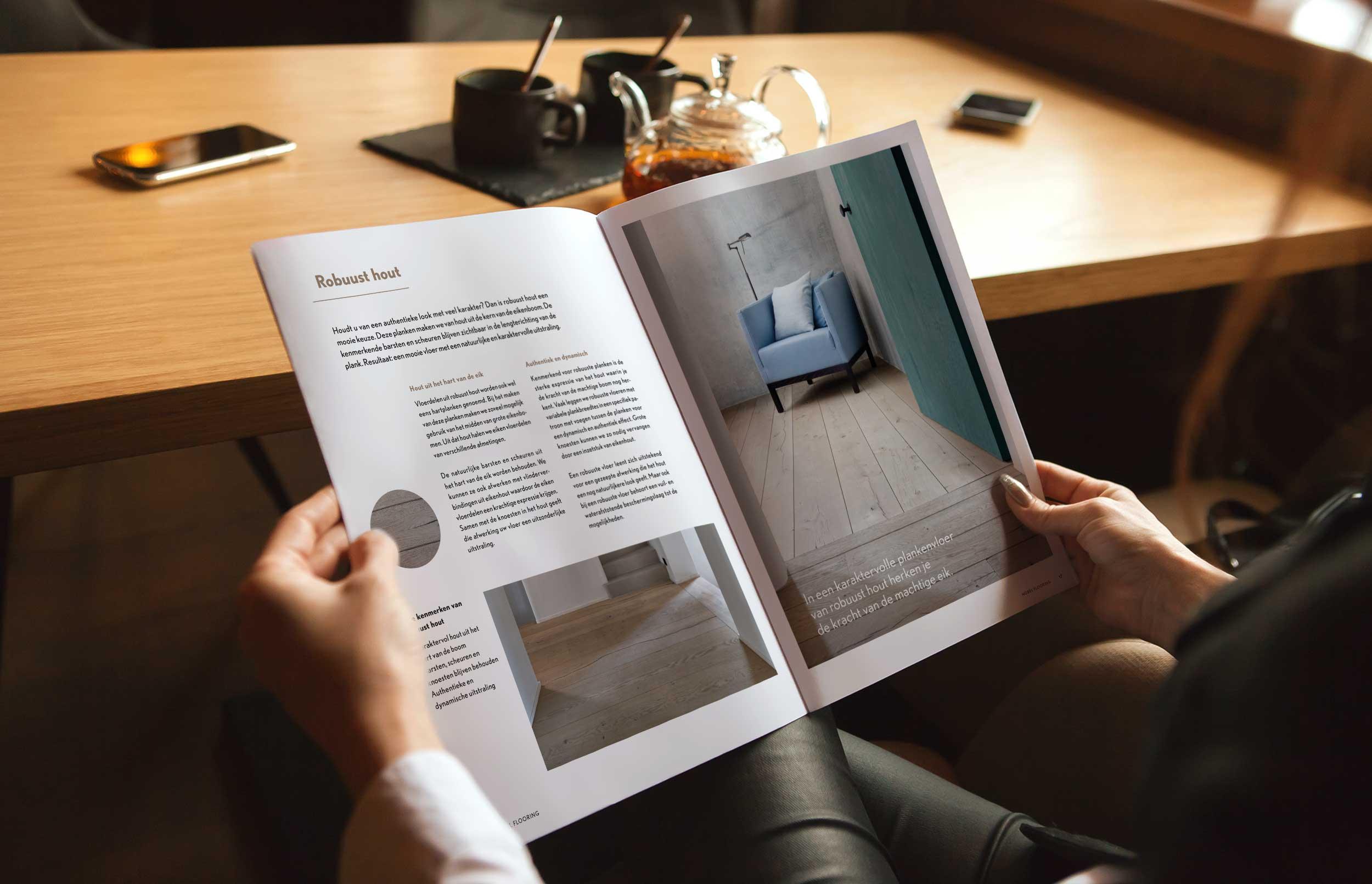 Brandle - Copywriting voor brochure van Nobel Flooring Persoon bladert door een brochure over houten vloeren aan een houten tafel, met foto’s van interieurtoepassingen en materiaalinformatie.