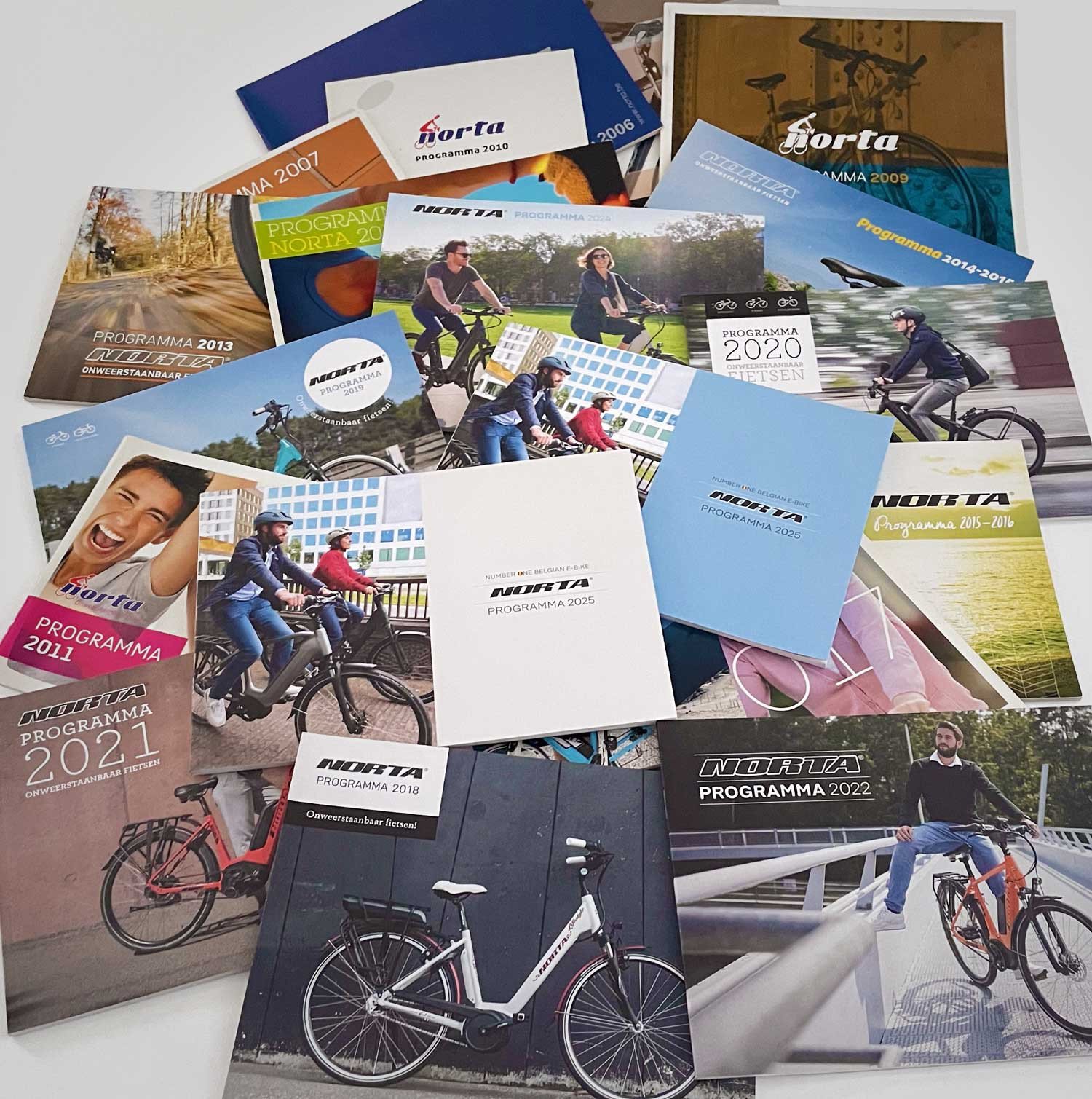 Overzicht van Norta-fietscatalogi uit verschillende jaren, verspreid op een oppervlak en met diverse coverontwerpen.
