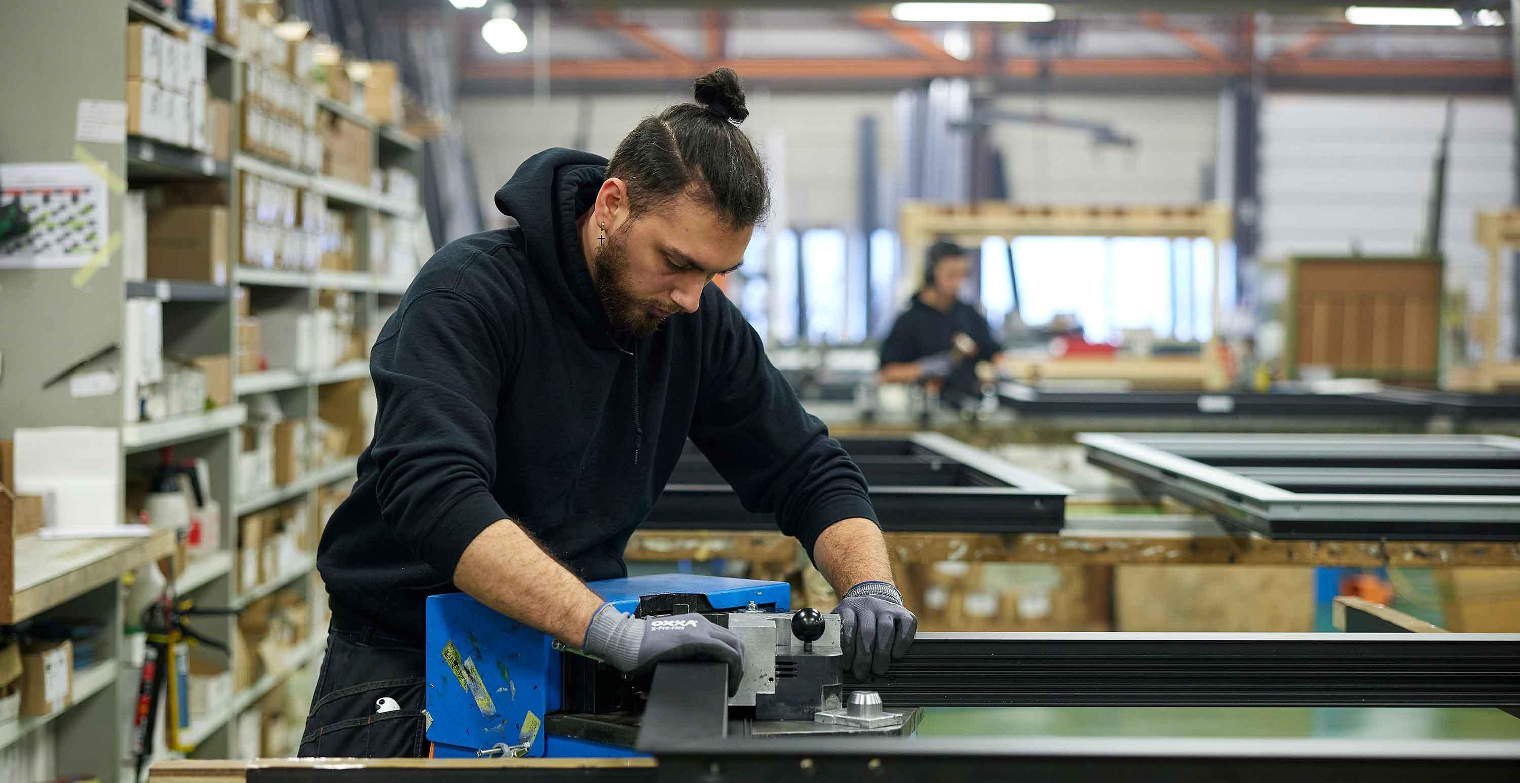 Brandle - Bedrijfsfotografie voor RaamSelect Medewerker werkt geconcentreerd aan een machine in een productiehal, omringd door metalen profielen en industriële apparatuur.