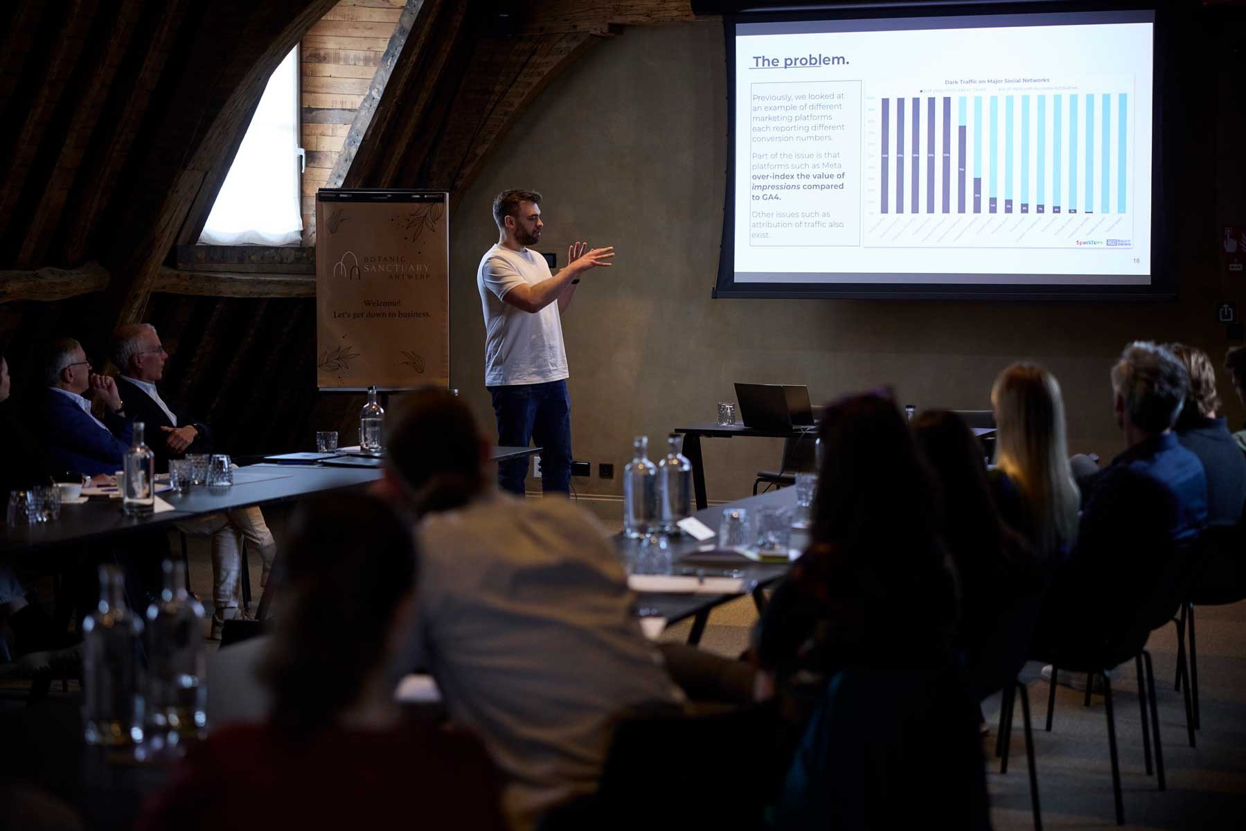 Spreker geeft een presentatie aan een publiek tijdens een S1 Inspires-event, met grafieken op het projectiescherm.